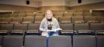 smiling college student sitting in auditorium with open textbook