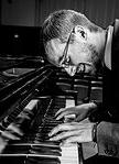 black & white image of smiling Corey Kendrick playing piano