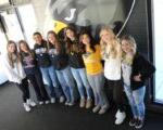 8 softball players standing in press box in front of hawk logo